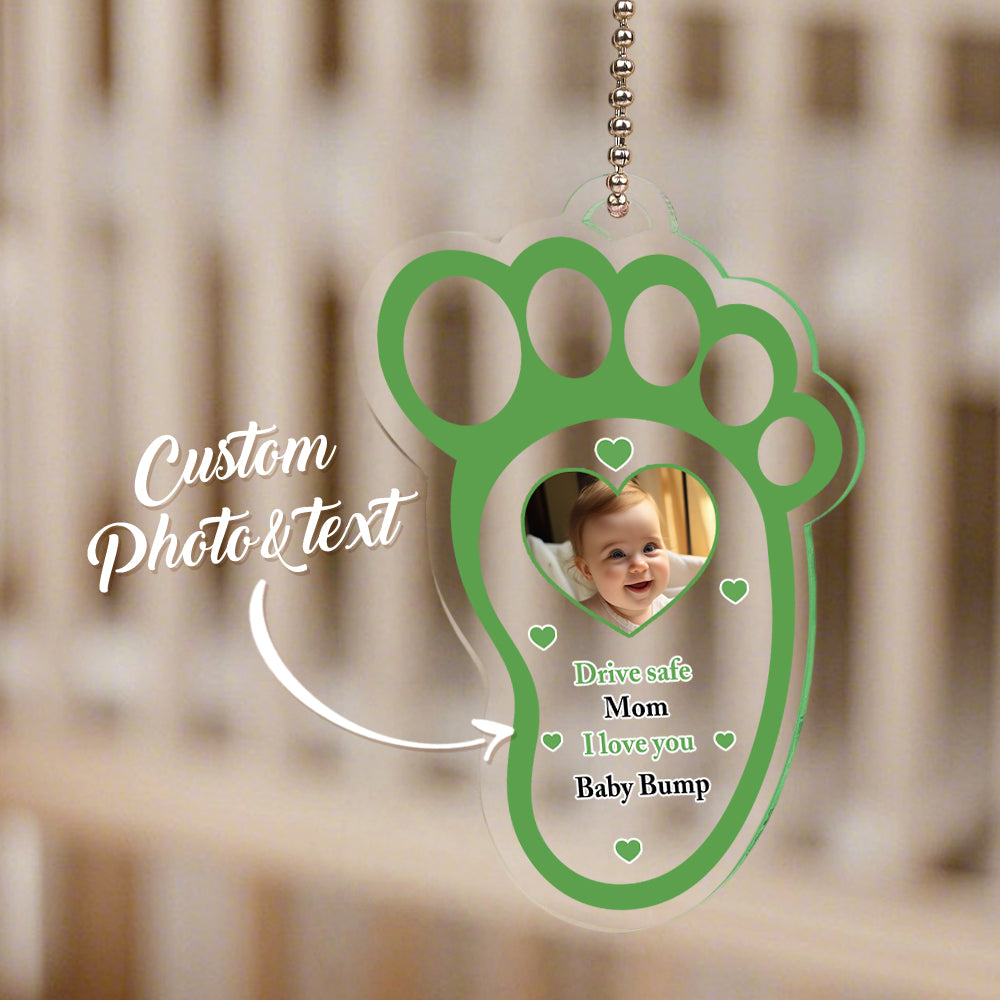 The baby footprint acrylic car mirror hanger mounted on a rear-view mirror in a car.