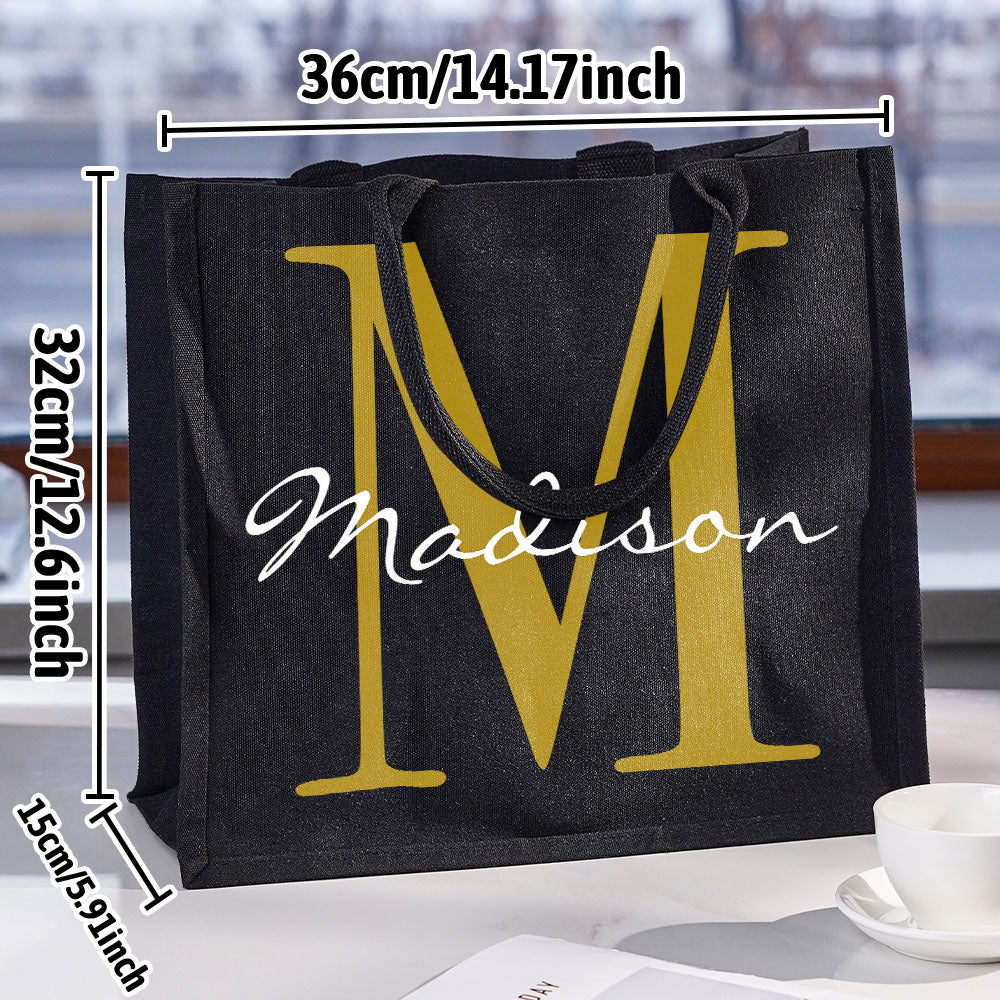 Flat lay of personalised black canvas tote filled with everyday items to demonstrate roomy capacity and practical use as a personalised gift