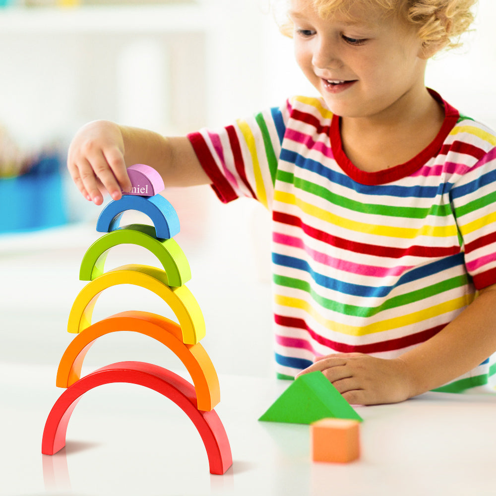 Scale view with hand for size reference: handmade Montessori wooden rainbow stacker pieces in subdued earth colours