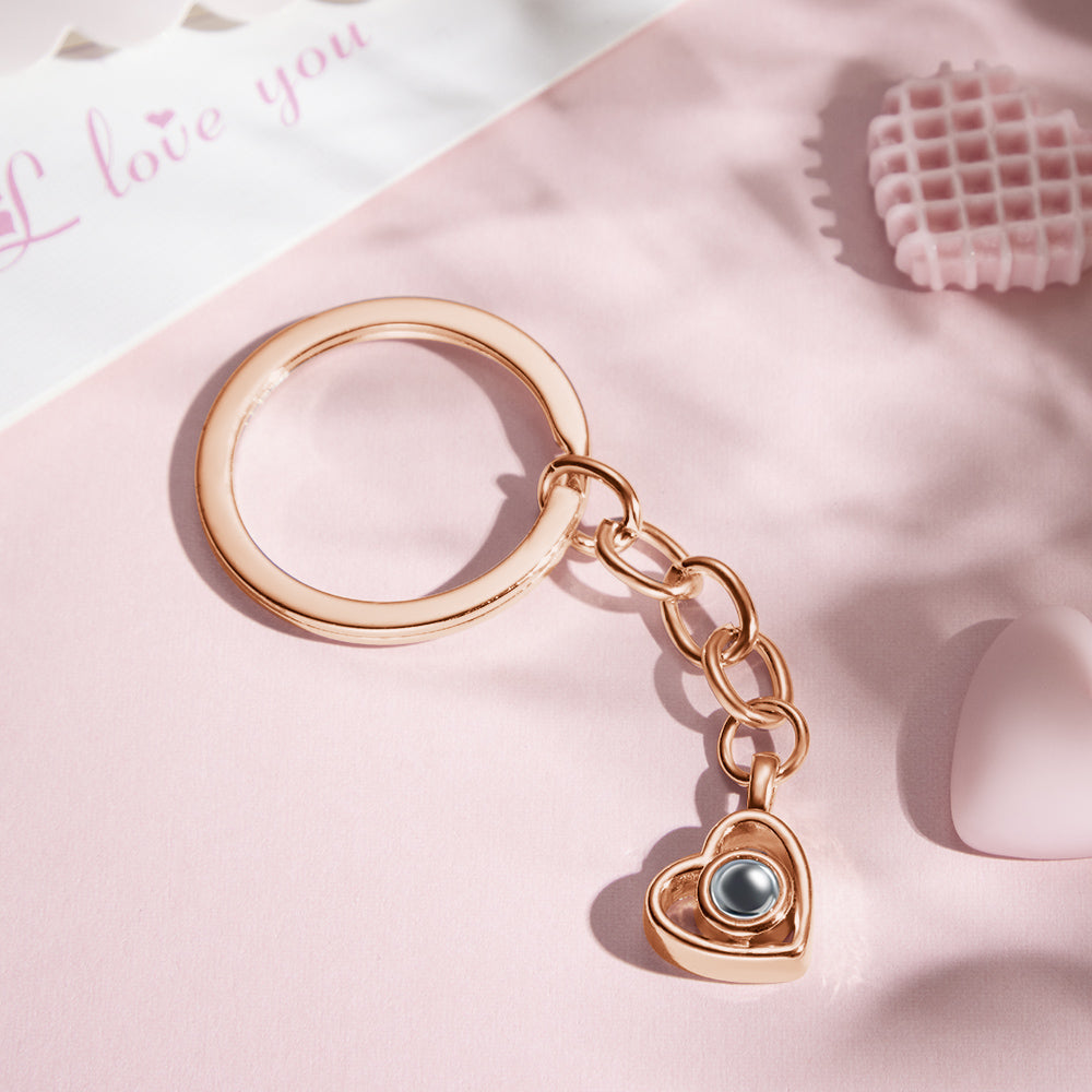 Heart-shaped projection keychain demonstrating a tiny projected photograph on a flat surface using a phone torch