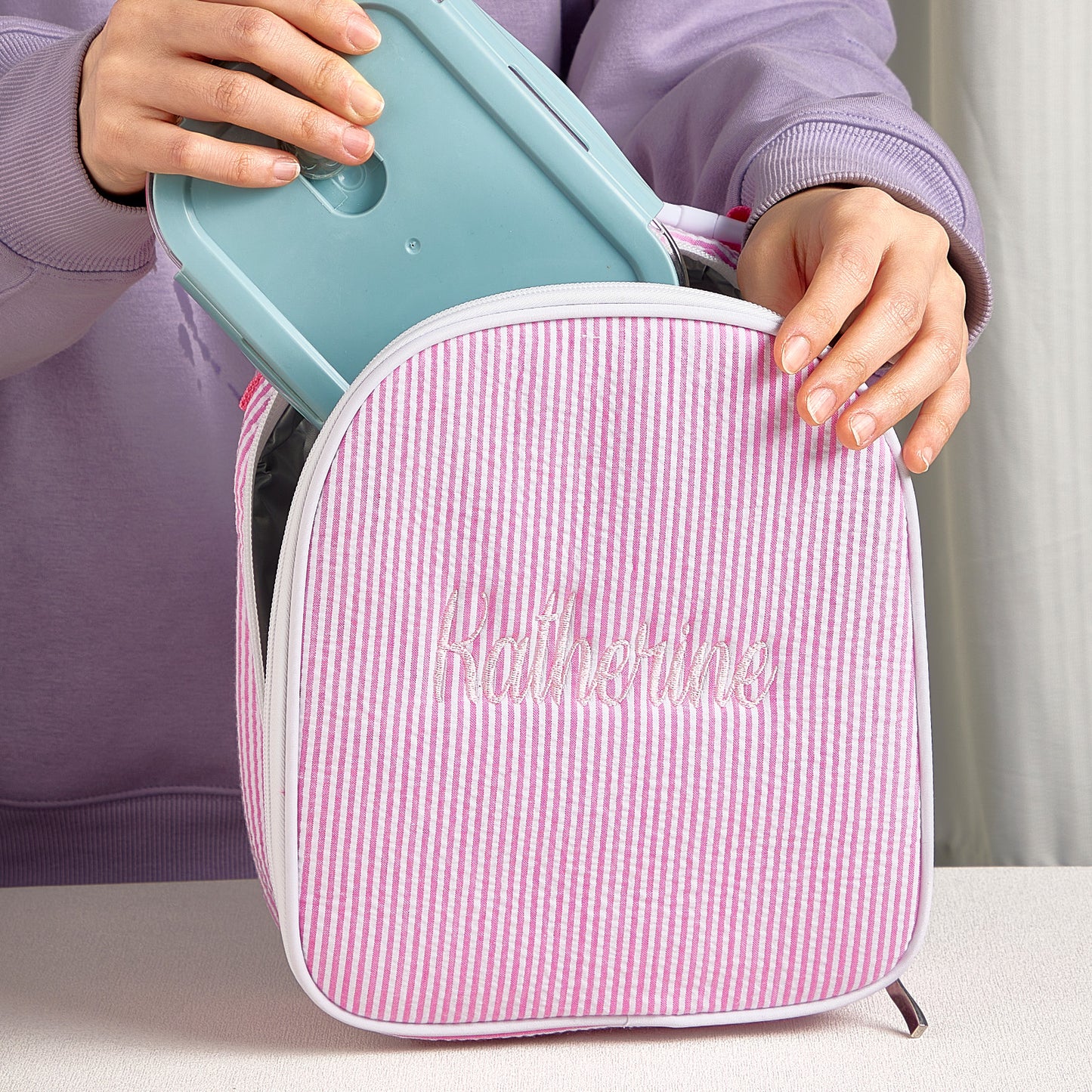 Angled view of personalised seersucker lunch bag showing compact shape and neat embroidered name — ideal school lunch bag