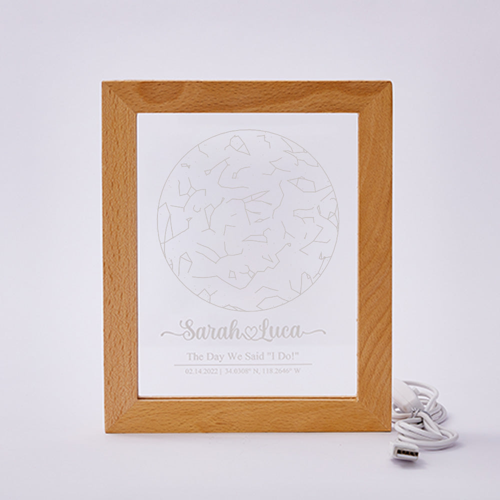 Personalised star map night lamp illuminated in a dark room — warm LED ambience from a USB-powered engraved acrylic plaque in a wood frame
