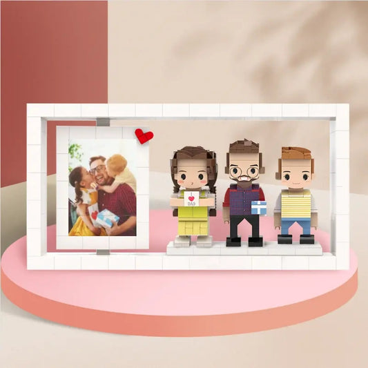 Customisable full‑body brick figures photo frame showing three personalised mini brick figures posed on a base with a photo background — bespoke three‑person custom figure frame and personalised wedding or family gift.
