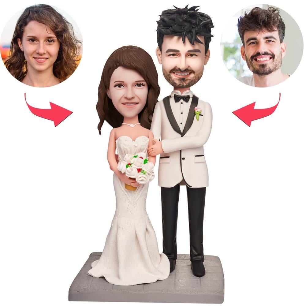 Two personalised polymer clay wedding bobbleheads of a couple lying in bed with engraved text on the base – handcrafted custom wedding keepsake for newlyweds