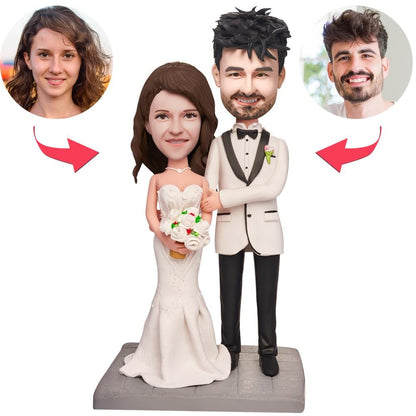 Two personalised polymer clay wedding bobbleheads of a couple lying in bed with engraved text on the base – handcrafted custom wedding keepsake for newlyweds