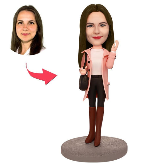 Personalised polymer clay bobblehead of a girl in an overcoat with engraved base text, customised head showing chosen hairstyle and facial expression
