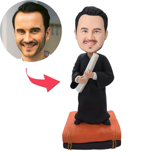 Personalised male graduate bobblehead in gown holding books with engraved name on base — handcrafted polymer clay keepsake, custom head and hairstyle