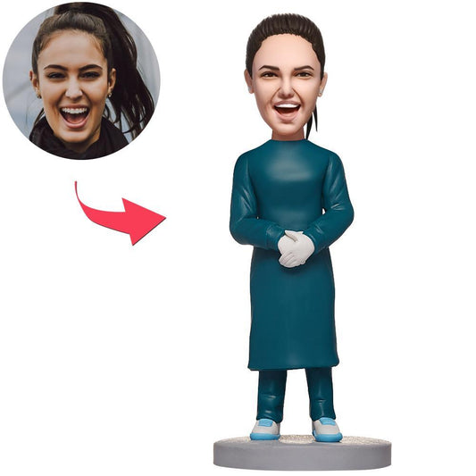 Front view of personalised female doctor bobblehead in operating room attire, polymer clay surgeon figurine with custom head and engraved text on the base — personalised surgeon gift