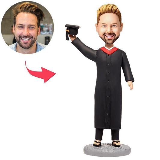 Personalised male graduate bobblehead in polymer clay wearing gown and mortarboard with engraved name on base — bespoke graduation keepsake with customised head from photo
