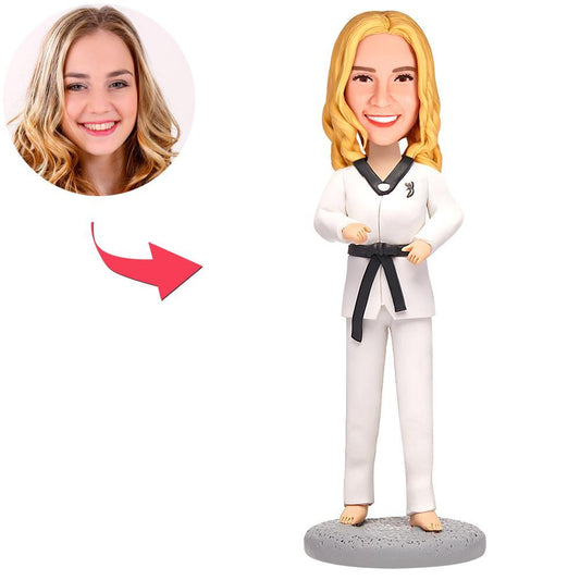Personalised female taekwondo bobblehead in white dobok with black belt, hand-crafted polymer clay figurine standing on an engraved wooden base — custom bobblehead, ideal personalised taekwondo gift.
