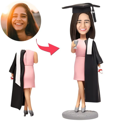 Personalised female graduate bobblehead in skirt wearing mortarboard, polymer clay bobblehead with a custom head from your photo and engraved base for name or message — ideal personalised graduate bobblehead gift.