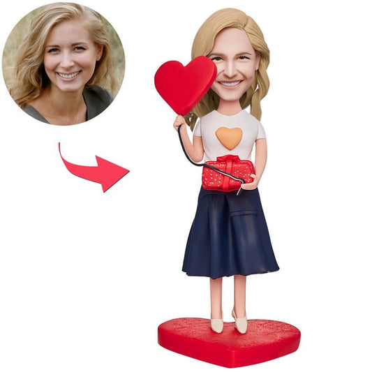 Hand-crafted polymer clay personalised bobblehead of a beautiful girl holding a gift box and love heart with engraved base for custom text, ideal romantic keepsake