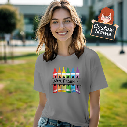 Flatlay of personalised crayon teacher T-Shirt folded to display the colourful crayon graphic and custom name – thoughtful personalised teacher gift for Back to School