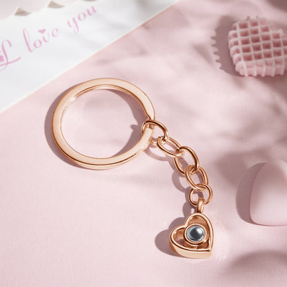 Heart-shaped projection keychain demonstrating a tiny projected photograph on a flat surface using a phone torch